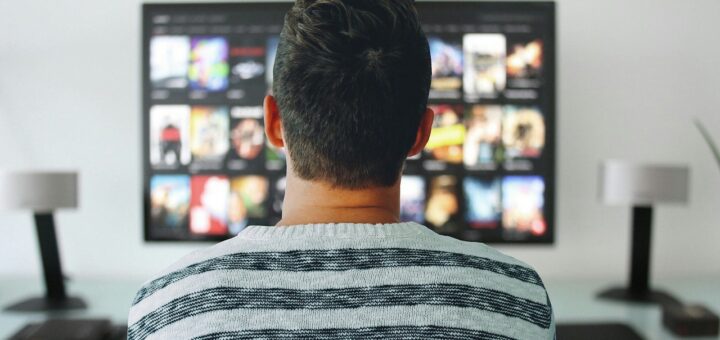 Um homem sentado à frente da TV escolhendo filmes para assistir